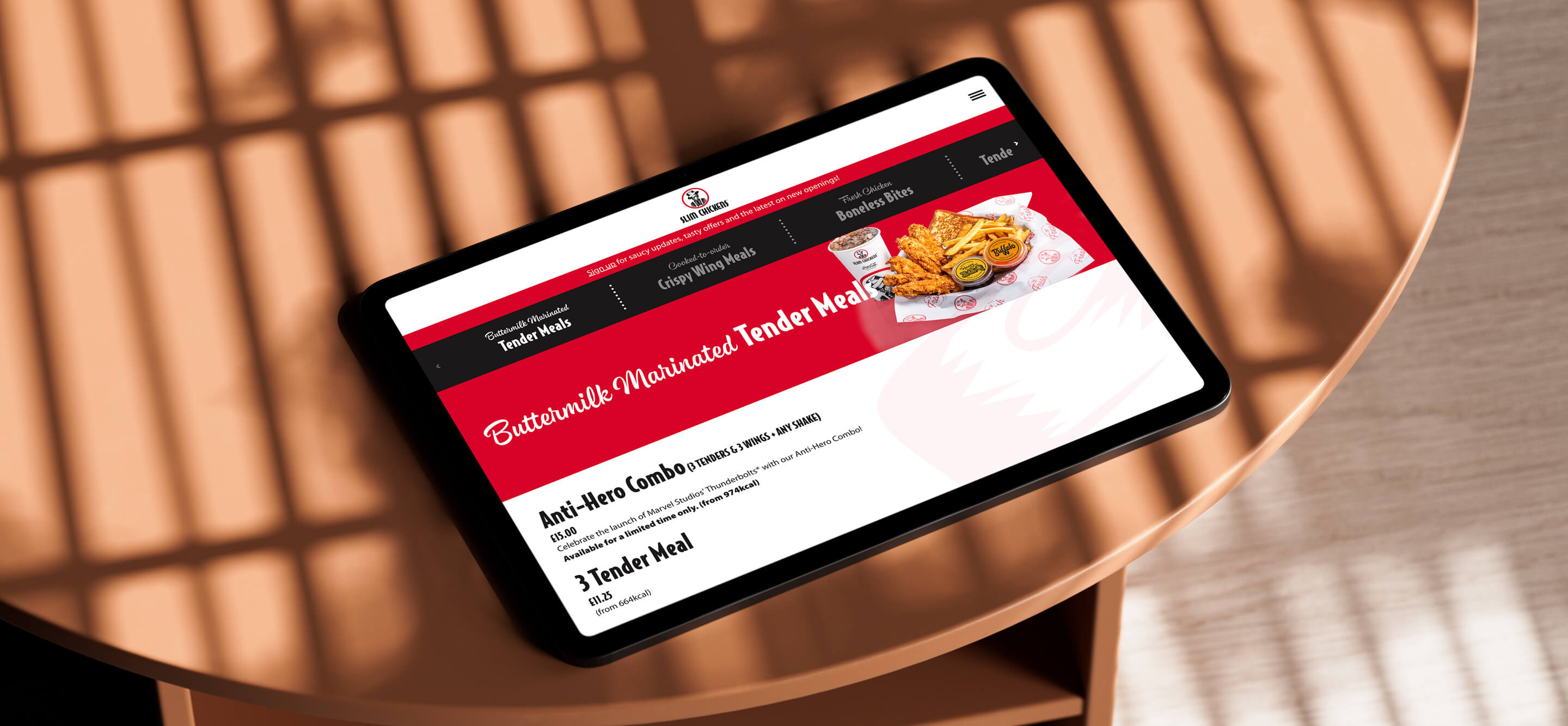 An image of the Slim Chickens App page on a tablet that is lying on a wooden table.